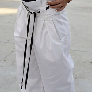 May include: White high-waisted pants with a black ribbon tie and a single front pocket.