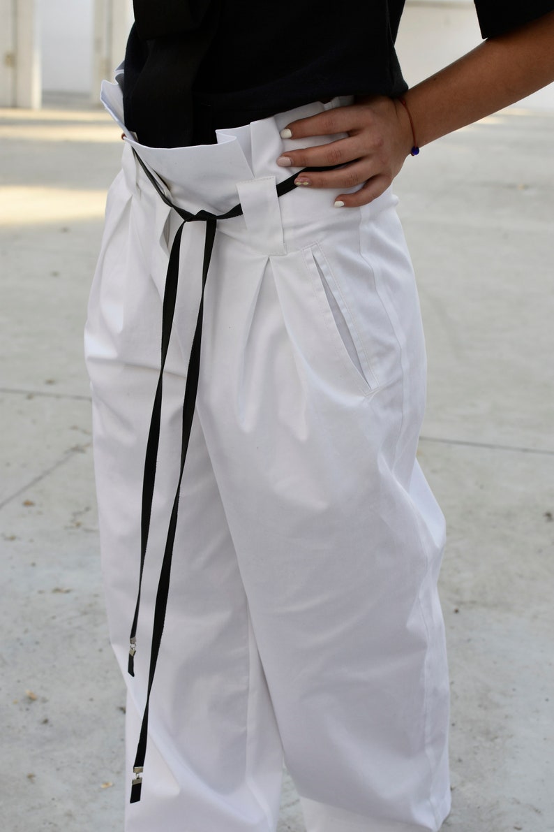 May include: White high-waisted pants with a black ribbon tie and a single front pocket.