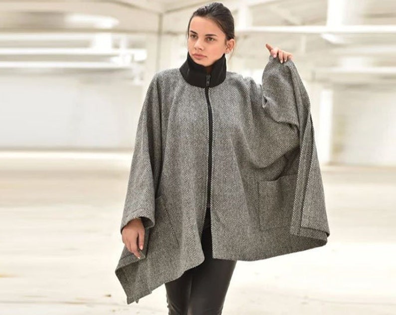 May include: A gray and black herringbone patterned poncho with a zipper closure and a pocket on the front.