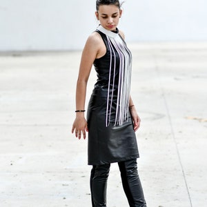 May include: A woman wearing a black leather dress with a white fringe detail and black leather boots.