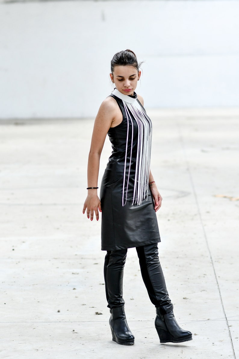 May include: A woman wearing a black leather dress with a white fringe detail and black leather boots.