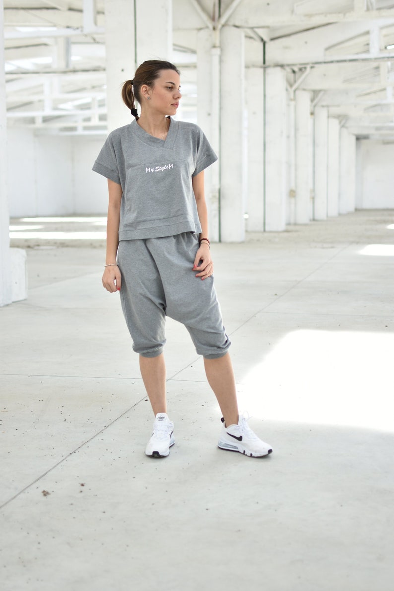 May include: A woman wearing a gray, cropped sweatshirt with the text "My Style" and matching gray sweatpants. She is wearing white sneakers with black accents.