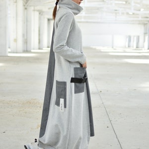 Puede incluir: Un vestido largo de manga larga gris y negro con cuello alto y cintur&oacute;n. El vestido tiene un bolsillo grande en la parte delantera y un bolsillo m&aacute;s peque&ntilde;o en el lateral. El vestido est&aacute; hecho de una tela suave y c&oacute;moda.
