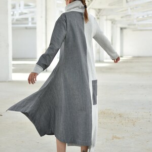 Puede incluir: Un vestido largo, gris y blanco con cuello alto y mangas largas. El vestido tiene un dobladillo asim&eacute;trico y fluido. La modelo lleva zapatillas blancas.