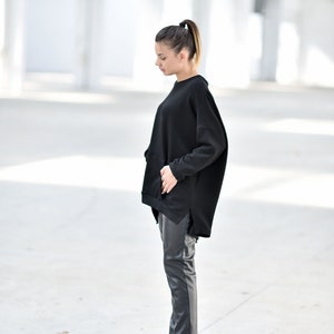 May include: A woman wearing a black oversized sweatshirt with a side slit and black leather pants. She is wearing black wedge boots.