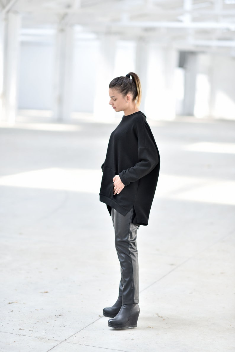 May include: A woman wearing a black oversized sweatshirt with a side slit and black leather pants. She is wearing black wedge boots.