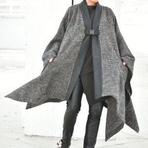 Pu&ograve; includere: Un cappotto a quadri bianco e nero con una cintura e fibbia nere. Il cappotto &egrave; indossato sopra un dolcevita nero e pantaloni neri. La persona indossa scarpe platform nere con fibbie.