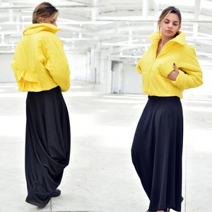 May include: A bright yellow cropped puffer jacket with a high collar and a ruffled hem detail, paired with a long, flowing black skirt. The jacket has a zipper closure and a puffy design. The outfit is set against a white background.
