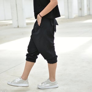 May include: A person wearing a black short-sleeved top and black pants with a loose fit. They are wearing silver sneakers.