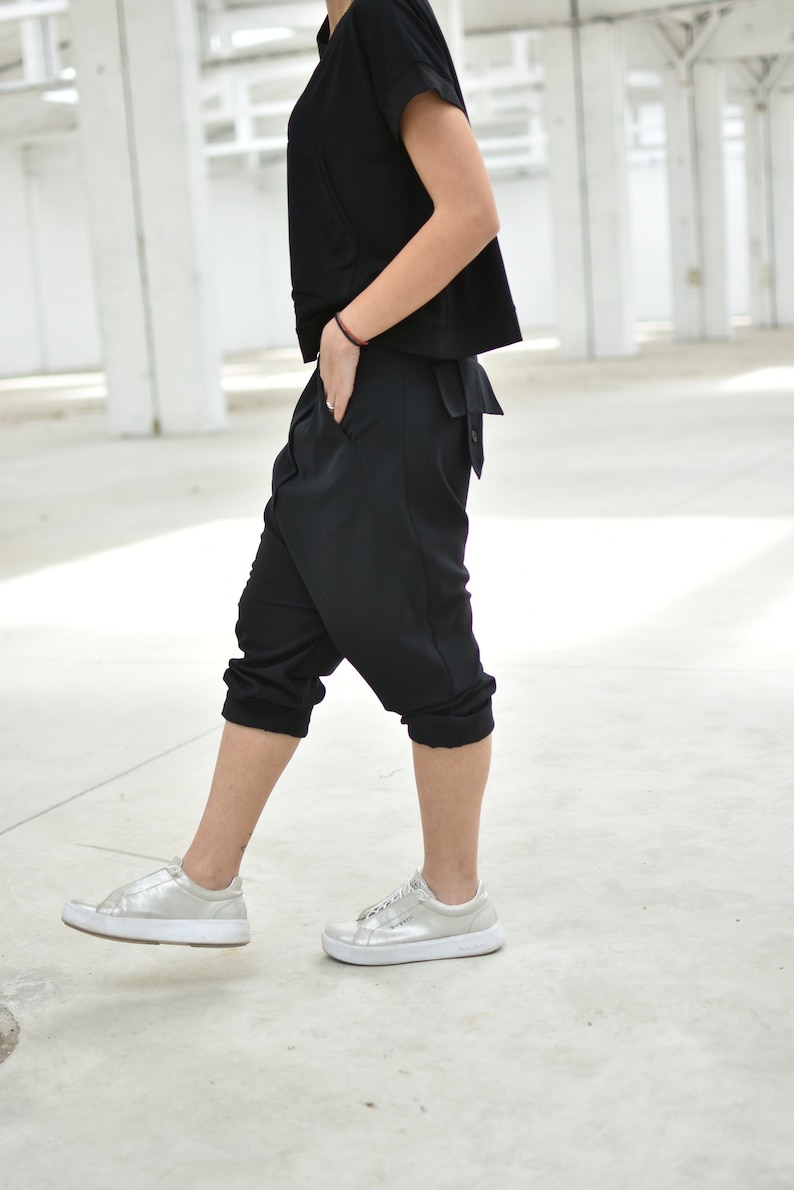 May include: A person wearing a black short-sleeved top and black pants with a loose fit. They are wearing silver sneakers.