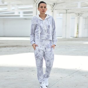 Puede incluir: Una sudadera con capucha gris de tie-dye y pantalones deportivos a juego con un cord&oacute;n blanco. La sudadera tiene una capucha blanca y una cremallera blanca.