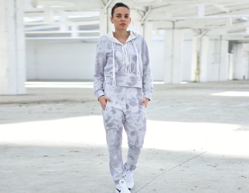 Puede incluir: Una sudadera con capucha gris de tie-dye y pantalones deportivos a juego con un cord&oacute;n blanco. La sudadera tiene una capucha blanca y una cremallera blanca.