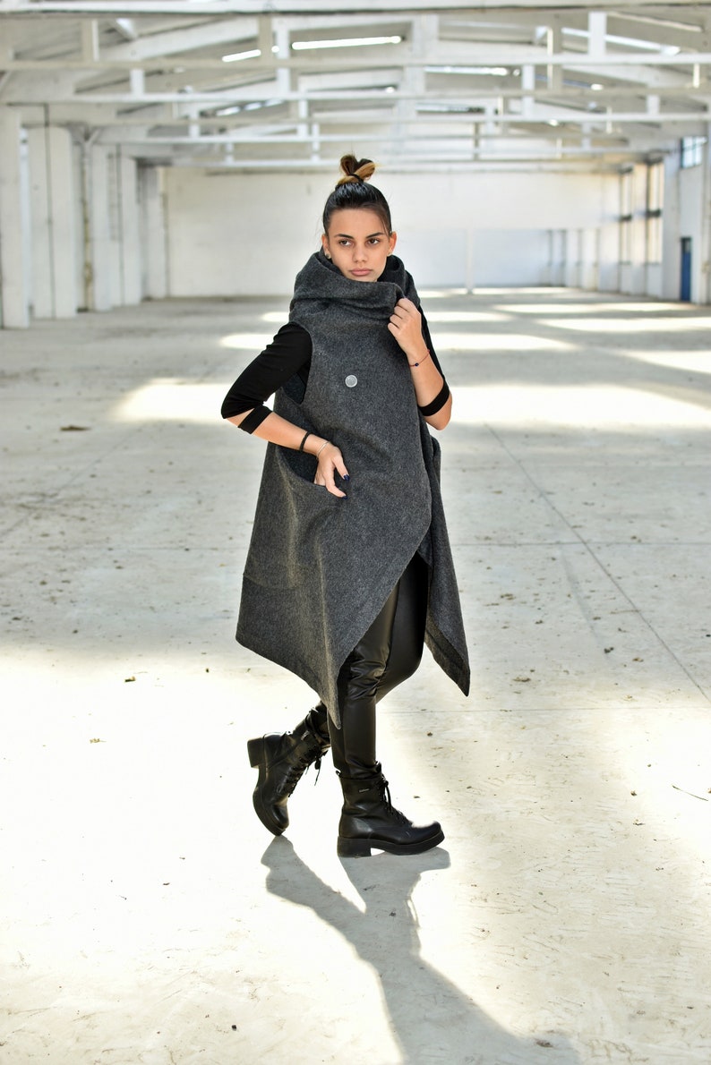 May include: A gray sleeveless coat with a high collar and a long, asymmetrical hem. The coat is made of a soft, textured fabric and has a relaxed fit.