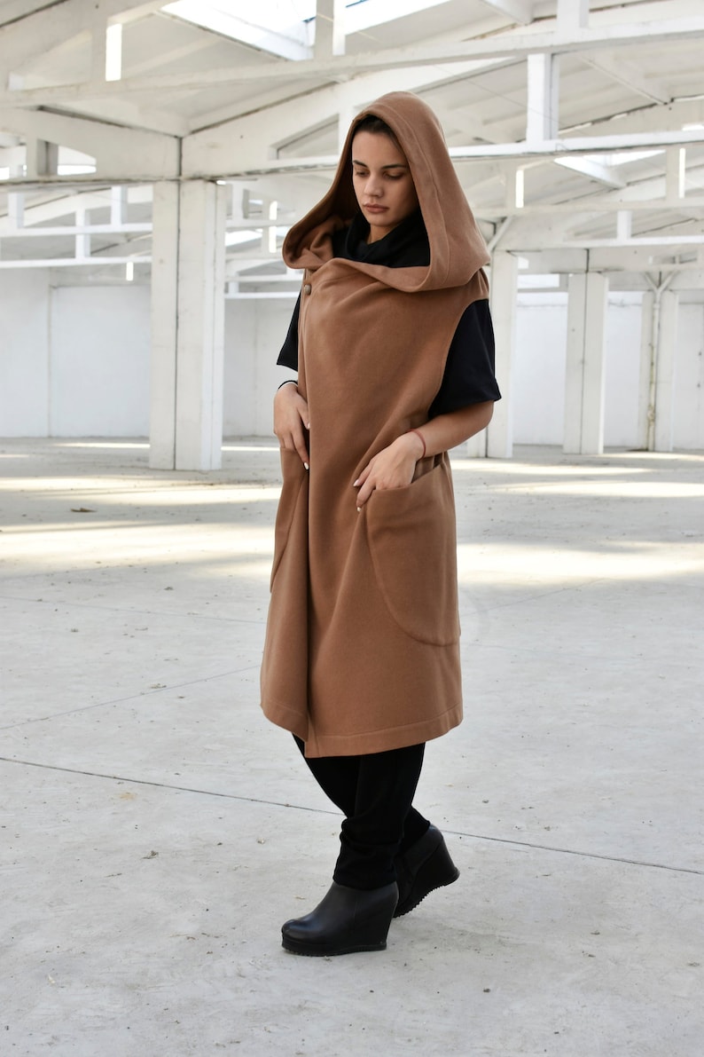 May include: A long brown hooded vest with large pockets. The vest is made of a soft, warm fabric and has a relaxed fit.