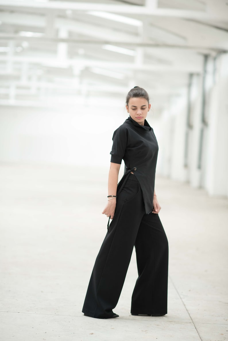 May include: A woman wearing a black mock neck top with a side tie detail and wide-leg black trousers.