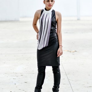 May include: A woman wearing a black leather dress with a white fringe collar and black leather boots.