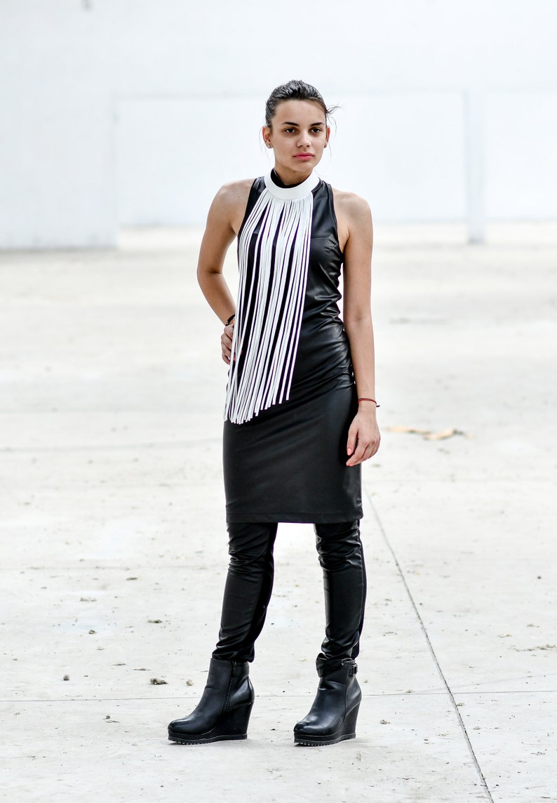 May include: A woman wearing a black leather dress with a white fringe collar and black leather boots.