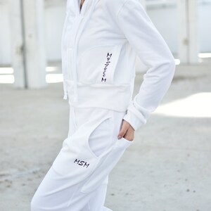 Puede incluir: Una sudadera con capucha blanca y pantalones de ch&aacute;ndal a juego con el texto "MSM" bordado en el bolsillo. La sudadera tiene una cremallera y una longitud recortada.