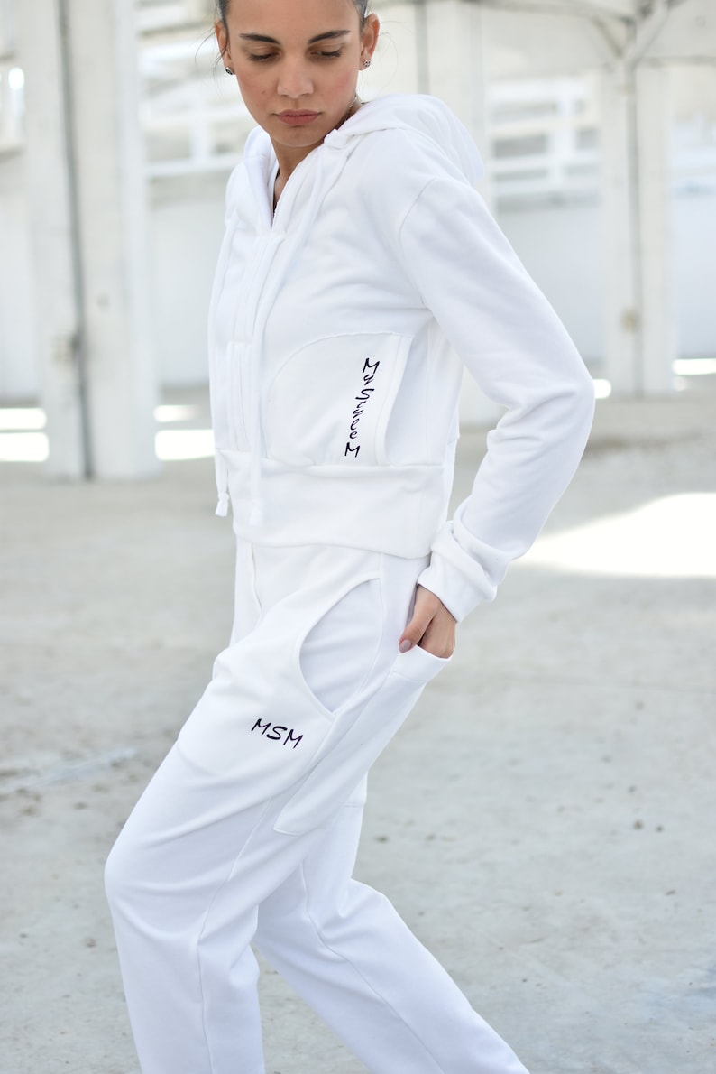 Puede incluir: Una sudadera con capucha blanca y pantalones de ch&aacute;ndal a juego con el texto "MSM" bordado en el bolsillo. La sudadera tiene una cremallera y una longitud recortada.