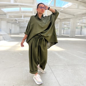 May include: A green linen pantsuit with a loose-fitting shirt and wide-leg pants. The shirt has a button-down collar and a single pocket on the left side. The pants have a tie at the waist and a relaxed fit.