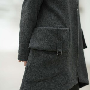 May include: A dark gray wool coat with a zipper closure and a large, angled pocket on the side. The pocket has a flap with a buckle closure.