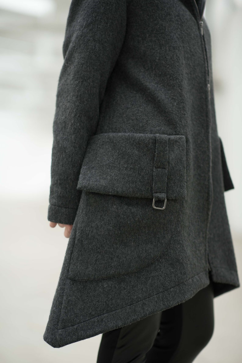 May include: A dark gray wool coat with a zipper closure and a large, angled pocket on the side. The pocket has a flap with a buckle closure.