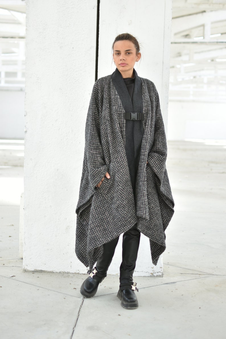 Pu&ograve; includere: Un lungo cappotto a quadri bianco e nero con una cintura e fibbia nere. Il cappotto &egrave; indossato sopra un dolcevita nero e pantaloni neri. La persona indossa scarpe nere con fibbie argentate.