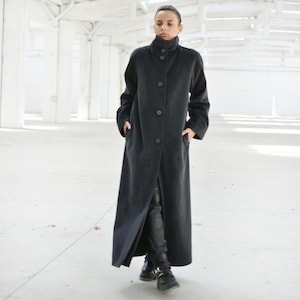Peut inclure: Un long manteau gris foncé avec un col montant et une rangée de boutons sur le devant. Le manteau est fait d'un tissu doux et chaud et a une coupe ample.