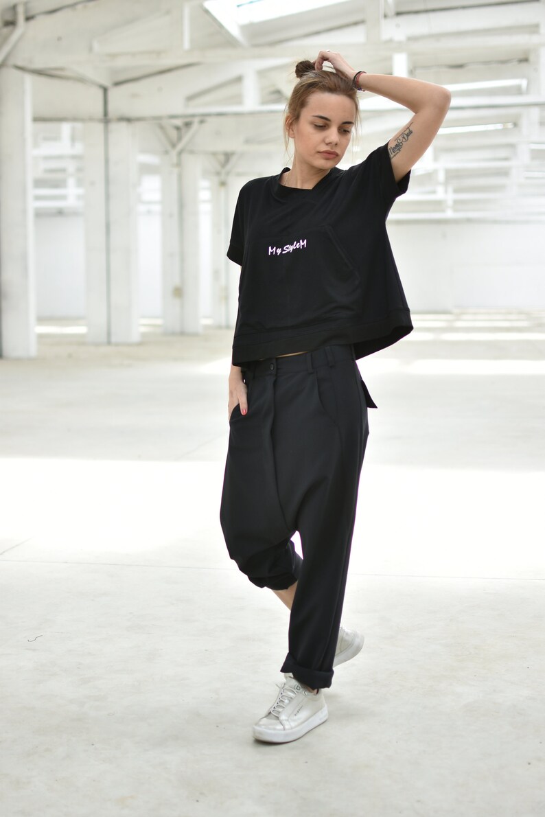 May include: A woman wearing a black cropped t-shirt with the text "My System" embroidered on the front, black pants, and white sneakers.