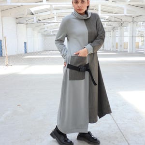 Puede incluir: Un vestido largo, gris y marr&oacute;n con un cintur&oacute;n negro y un bolsillo grande en el lateral. El vestido tiene cuello alto y mangas largas.