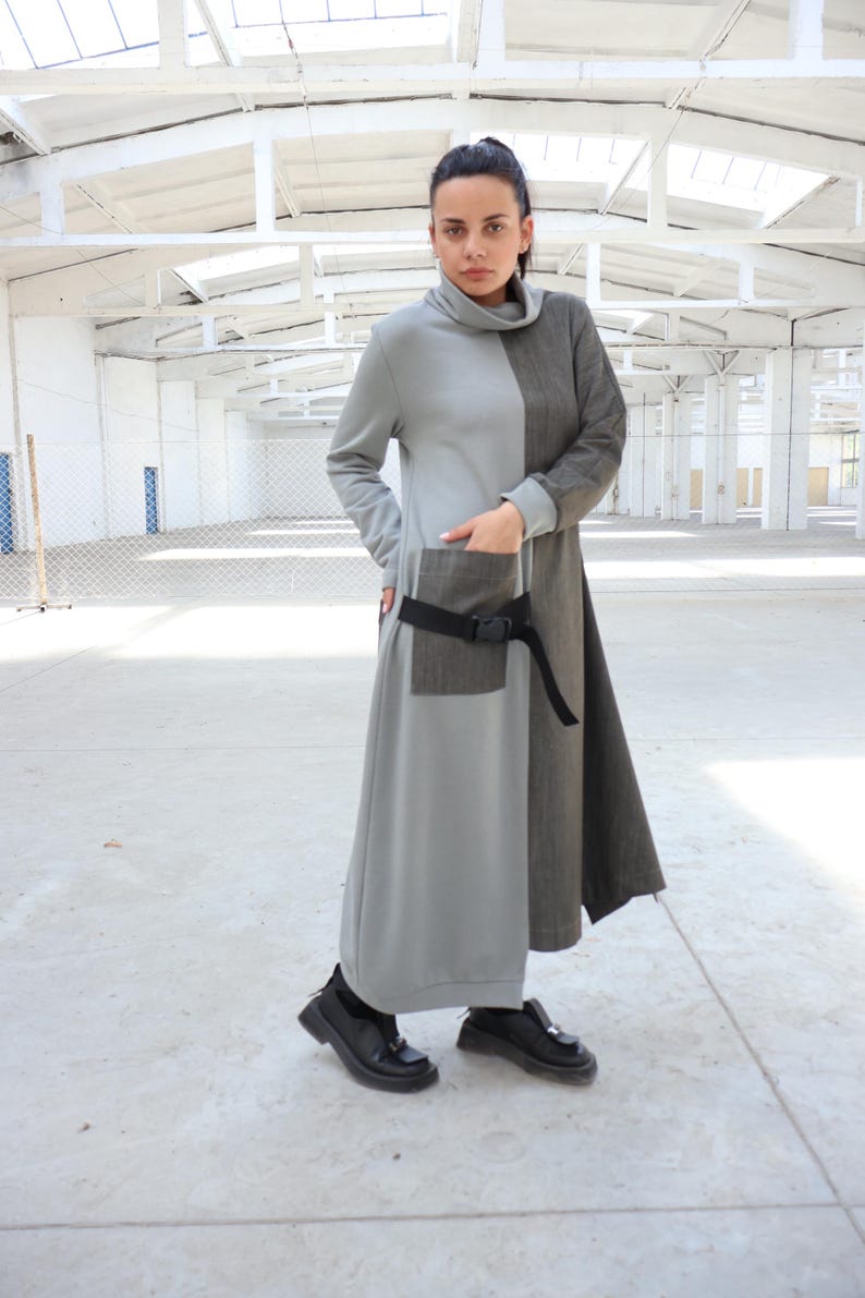 Puede incluir: Un vestido largo, gris y marr&oacute;n con un cintur&oacute;n negro y un bolsillo grande en el lateral. El vestido tiene cuello alto y mangas largas.