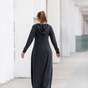 May include: A woman wearing a long, gray hooded dress with a relaxed fit. The dress has a slightly textured fabric and is worn with a ponytail.