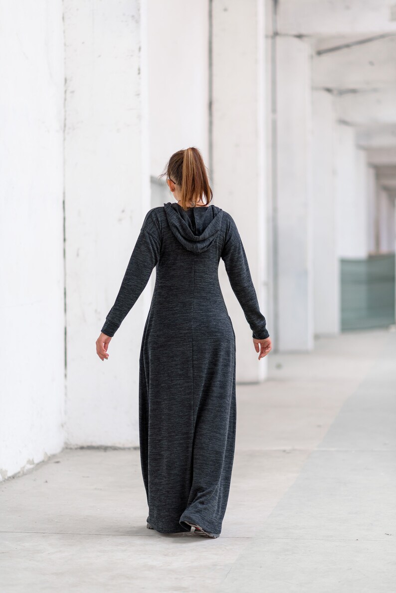May include: A woman wearing a long, gray hooded dress with a relaxed fit. The dress has a slightly textured fabric and is worn with a ponytail.