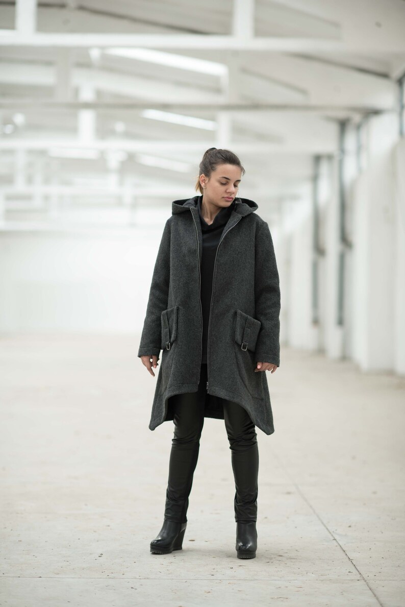 May include: A woman wearing a long, gray hooded coat with a zipper closure and two pockets. She is wearing black pants and black boots.