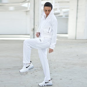 Puede incluir: Una sudadera con capucha blanca y pantalones deportivos a juego con la palabra "HSM" impresa en la pierna izquierda y "24/7" impresa en la manga derecha.