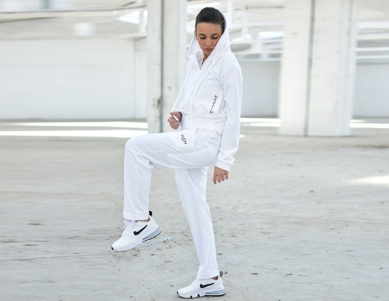 Puede incluir: Una sudadera con capucha blanca y pantalones deportivos a juego con la palabra "HSM" impresa en la pierna izquierda y "24/7" impresa en la manga derecha.