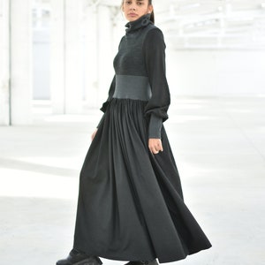 May include: A long black dress with a grey turtleneck top. The dress has a gathered skirt and long sleeves.