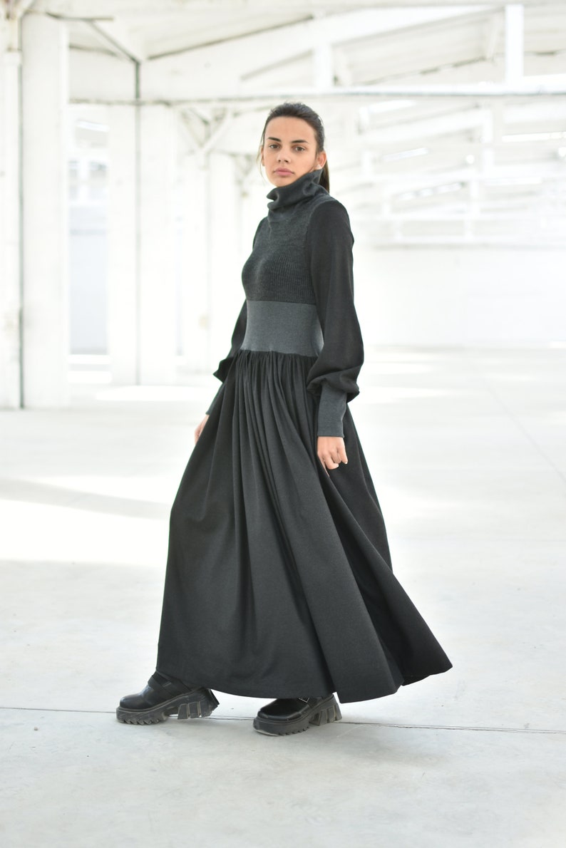 May include: A long black dress with a grey turtleneck top. The dress has a gathered skirt and long sleeves.