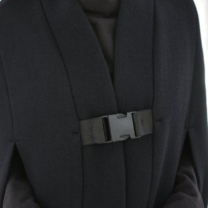 May include: A black cape with a black buckle closure. The cape has a wide collar and long sleeves.