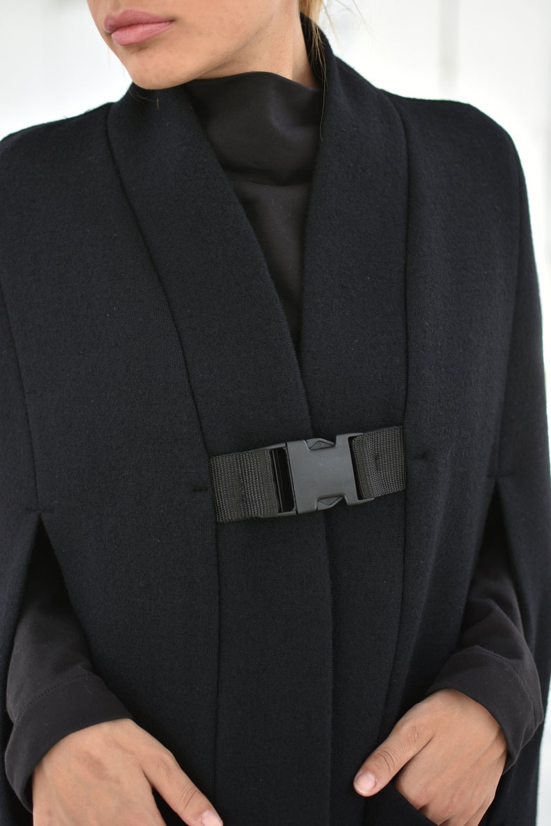 May include: A black cape with a black buckle closure. The cape has a wide collar and long sleeves.
