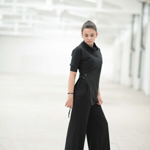May include: A woman wearing a black mock neck top with a side tie detail and black wide-leg trousers.