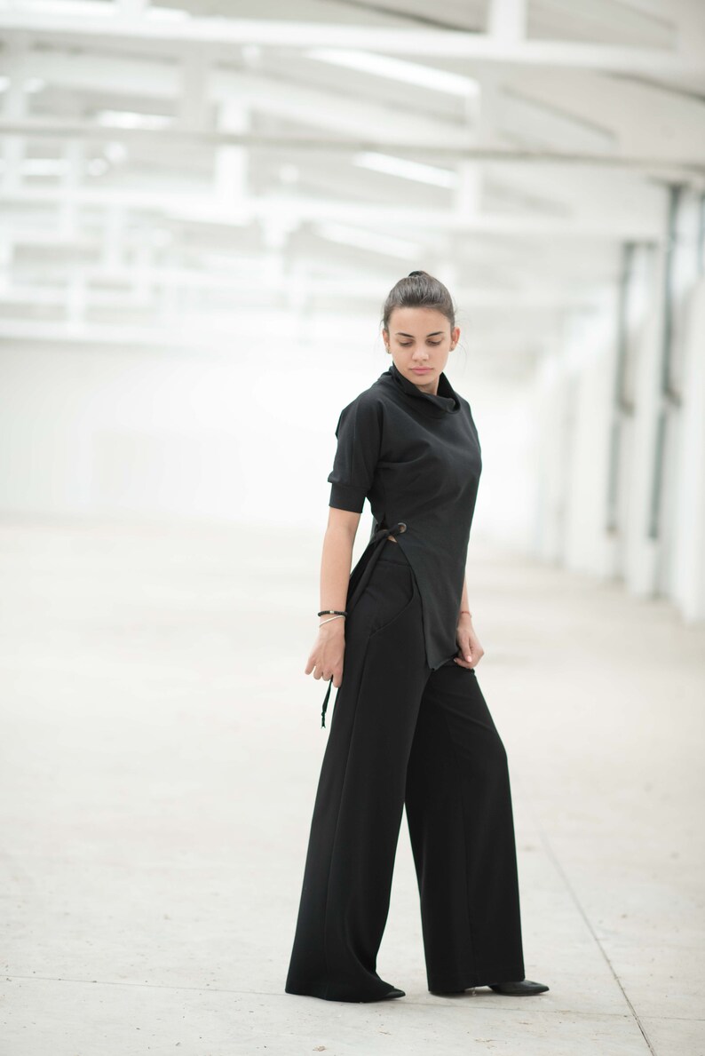 May include: A woman wearing a black mock neck top with a side tie detail and black wide-leg trousers.