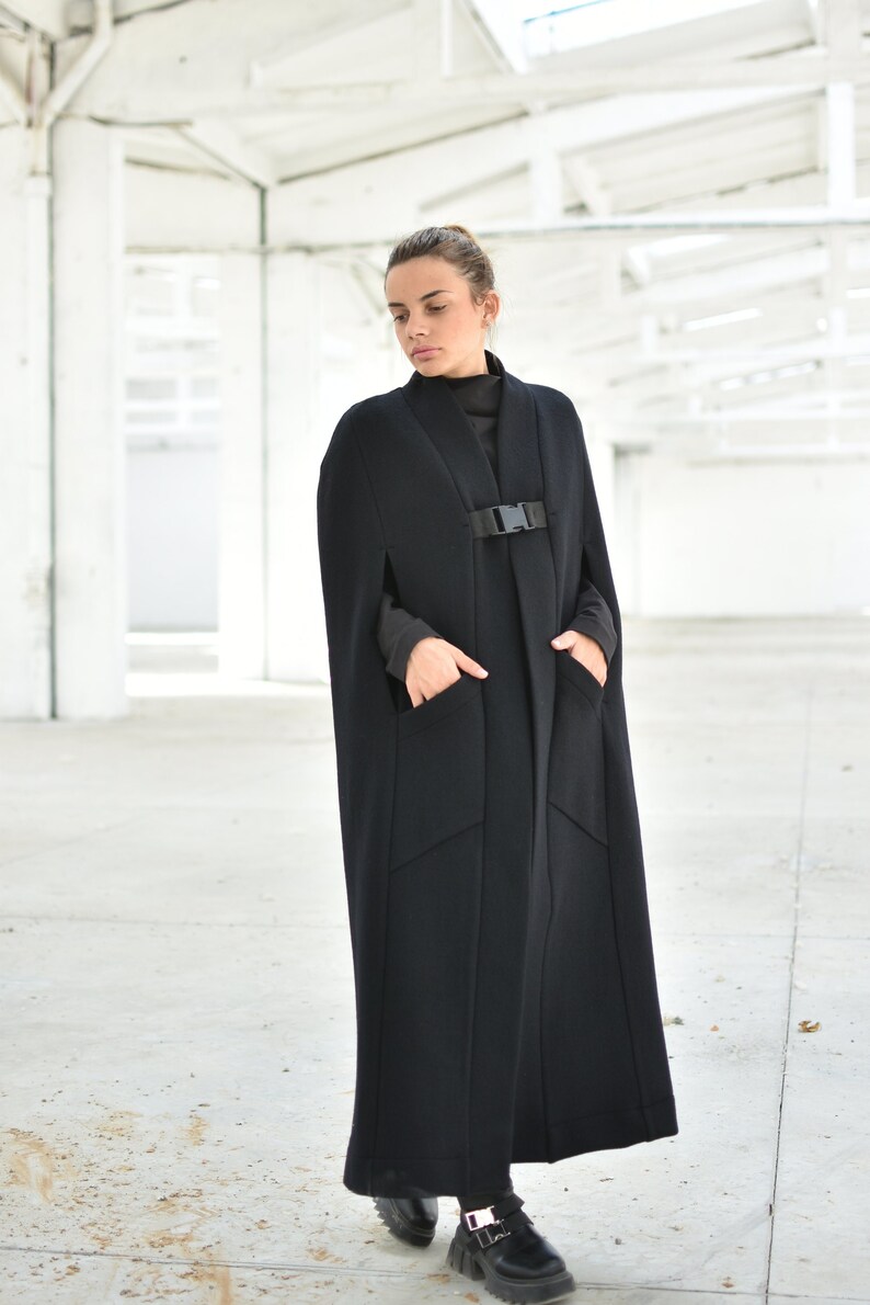 May include: A long black cape with a buckle closure and pockets. The cape is made of a thick, textured fabric.