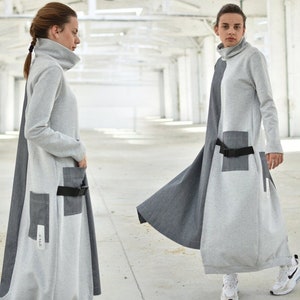 Puede incluir: Un vestido largo, gris y gris oscuro con cuello alto y cintur&oacute;n. El vestido tiene dos bolsillos grandes en la parte delantera y una peque&ntilde;a etiqueta con el texto "2-112" en el lado izquierdo.