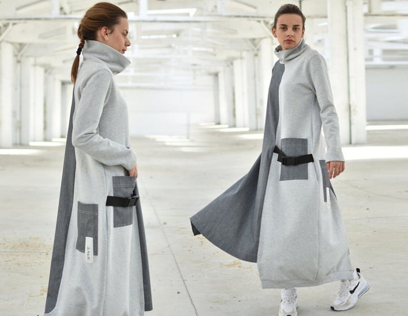 Puede incluir: Un vestido largo, gris y gris oscuro con cuello alto y cintur&oacute;n. El vestido tiene dos bolsillos grandes en la parte delantera y una peque&ntilde;a etiqueta con el texto "2-112" en el lado izquierdo.