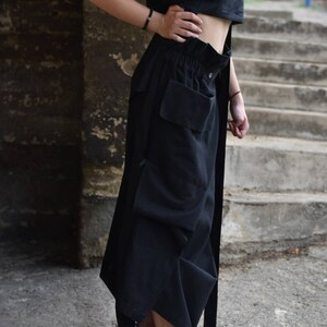 May include: A black sleeveless crop top and a black, long, flowing skirt with a large cargo pocket. The skirt has a drawstring waist and a belt. The person is wearing white sneakers.