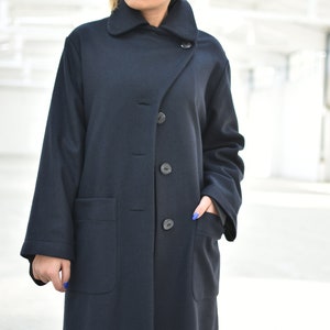 May include: A long, dark blue coat with a collar that can be worn up or down. The coat has a single button closure and two large pockets.