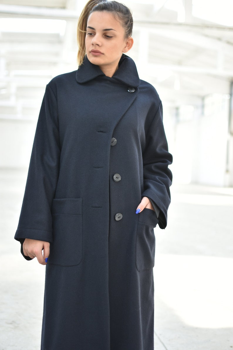 May include: A long, dark blue coat with a collar that can be worn up or down. The coat has a single button closure and two large pockets.