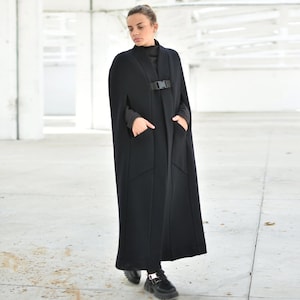 May include: A long black cape with a buckle closure and pockets. The cape is made of a soft, warm fabric and has a relaxed fit.