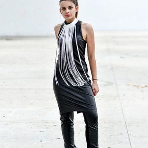May include: A woman wearing a black leather dress with a white fringe detail at the neckline. She is also wearing black leather trousers and black boots.